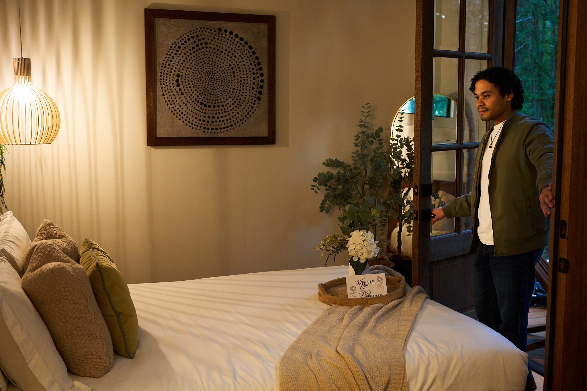 A guest enters a warmly lit bedroom prepared for the stay.