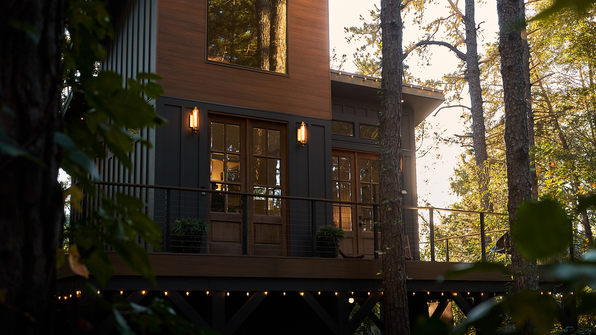 An illuminated treehouse exterior rises among tall trees at dusk.